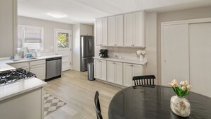 Une cuisine moderne avec des meubles blancs, des appareils en acier inoxydable et un coin repas comprenant une table et des chaises.