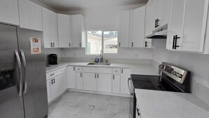 Una cocina moderna con armarios blancos, un refrigerador de acero inoxidable, un fregadero y una estufa.
