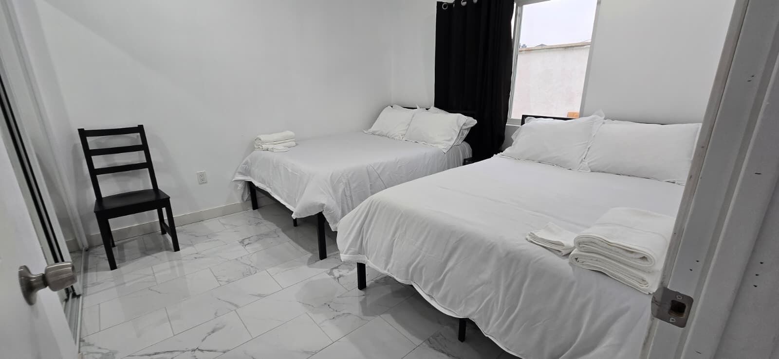 Une chambre d’hôtel avec deux lits simples, une chaise et une fenêtre avec des rideaux.