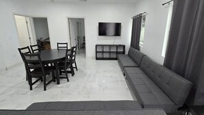Una sala de estar moderna con comedor, un sofá, un televisor y una ventana con cortinas.