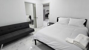 Habitación de hotel moderna con cama, sofá y baño visible a través de una puerta abierta.