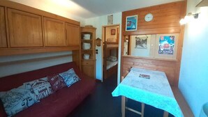 Et kompakt værelse med en rød sofa, træskabe, køjeseng og et lille bord med hvide blonde.'