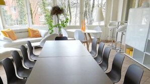A conference room with a long table and multiple chairs, large windows with a view of buildings, and a plant on the windowsill. - Bellevue (Porrentruy)
