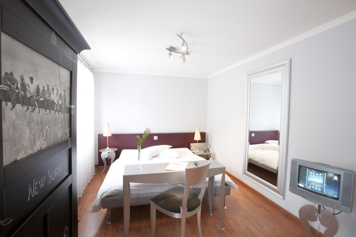 A hotel room with a bed, bedside tables, a desk, a chair, a TV, and a framed picture on the wall.