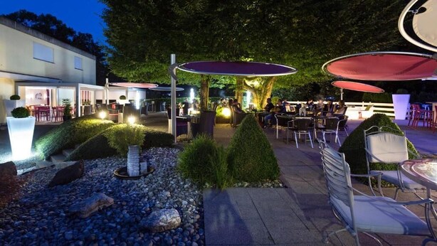 An outdoor patio area with tables and chairs, surrounded by a landscaped garden with rocks and plants. - Bellevue (Porrentruy)