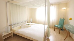 A bedroom with a four-poster bed, a bedside table with a lamp, a chair, and a desk with a lamp. - Bellevue (Porrentruy)