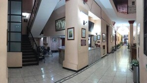 A spacious hotel lobby with a central staircase, a reception desk, and framed pictures on the walls. - Hotel San Angel Puebla (Puebla)