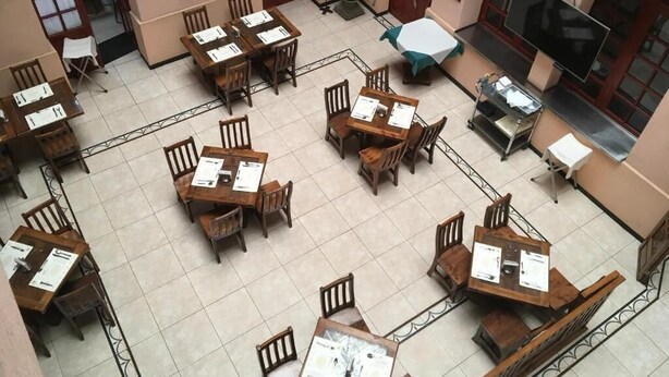 A hotel lobby with multiple wooden tables and chairs, a large TV screen, and a chandelier. - Hotel San Angel Puebla (Puebla)