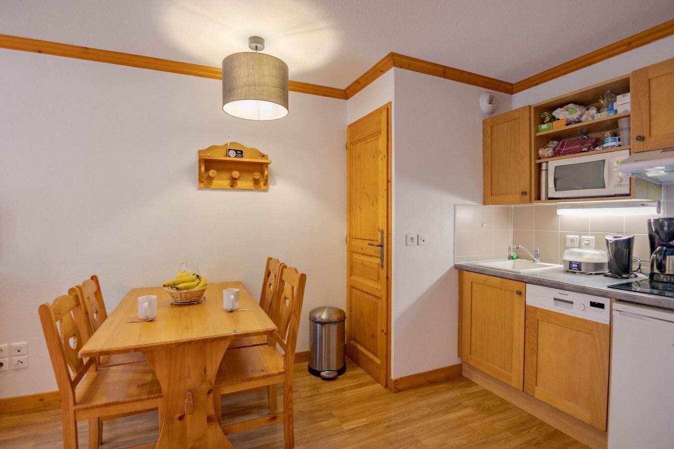 Eine kompakte Küche mit Holzausstattung, einer Mikrowelle, einer Kaffeemaschine und einem Essbereich mit Tisch und Stühlen.