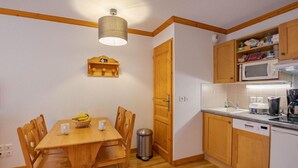 Eine kompakte Küche mit Holzausstattung, einer Mikrowelle, einer Kaffeemaschine und einem Essbereich mit Tisch und Stühlen.