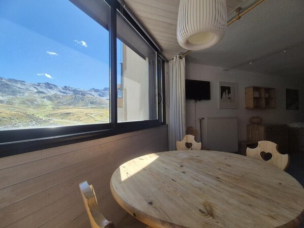 A room with a large window, a round wooden table, and a view of a mountainous landscape. - 200m from resort center, 3rd floor, tv, 40m², Val Thorens (Val Thorens)