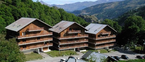 Un edificio de madera de varios pisos con balcones, rodeado de exuberante vegetación y montañas al fondo.