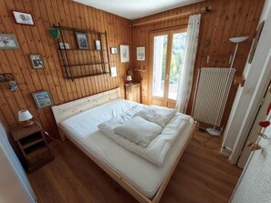 Une pièce aux murs lambrissés, avec un lit, une table de chevet et un radiateur.