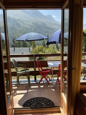 Un balcon avec vue sur les montagnes, deux parasols et du mobilier d’extérieur.