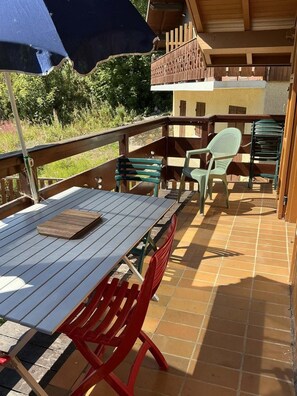 A wooden deck with a table and chairs, a blue umbrella, and a view of greenery. - Chalet, swimming pool, balcony, tv, ski locker, 80m², Valloire (Valloire)