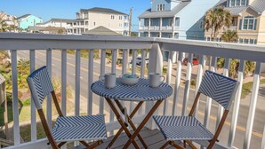 A balcony with two wicker chairs and a small table, overlooking a street with houses. - Beach Nest - R R Beach Club (North Myrtle Beach)