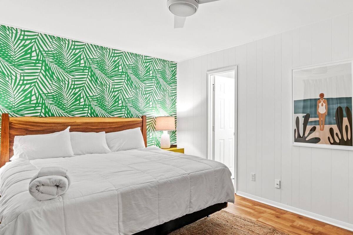 A bedroom with a bed, a nightstand, a lamp, a painting, and a door.