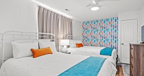 Hotellihuone, jossa on kaksi sänkyä, kattotuuletin, televisio ja kuviollinen seinä.