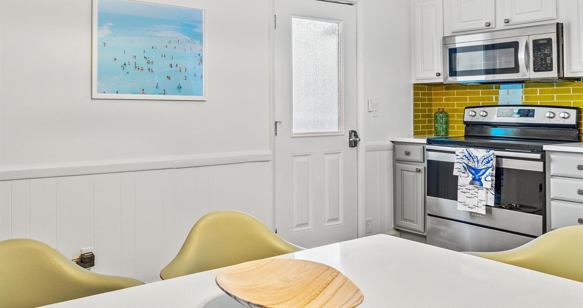 Une cuisine avec des meubles blancs, un four à micro-ondes, un four traditionnel et une table à manger avec des chaises.