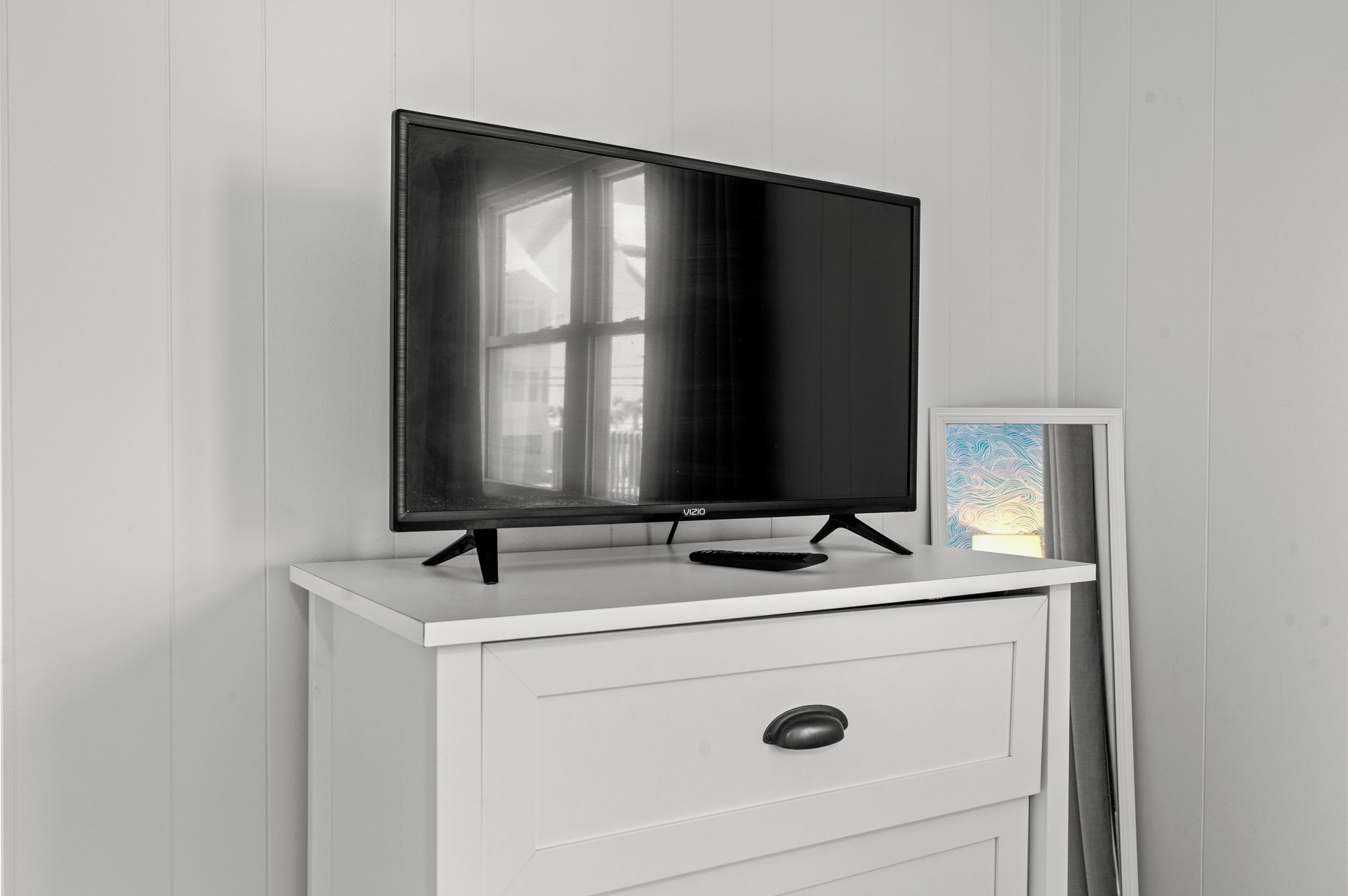 A flat-screen TV on a white TV stand with a remote control.