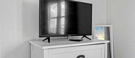 A flat-screen TV on a white TV stand with a remote control.