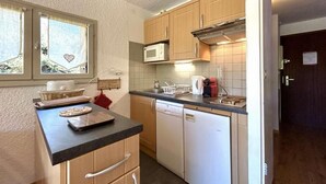 A compact kitchen with wooden cabinets, a microwave, a dishwasher, and a window with a heart decoration.