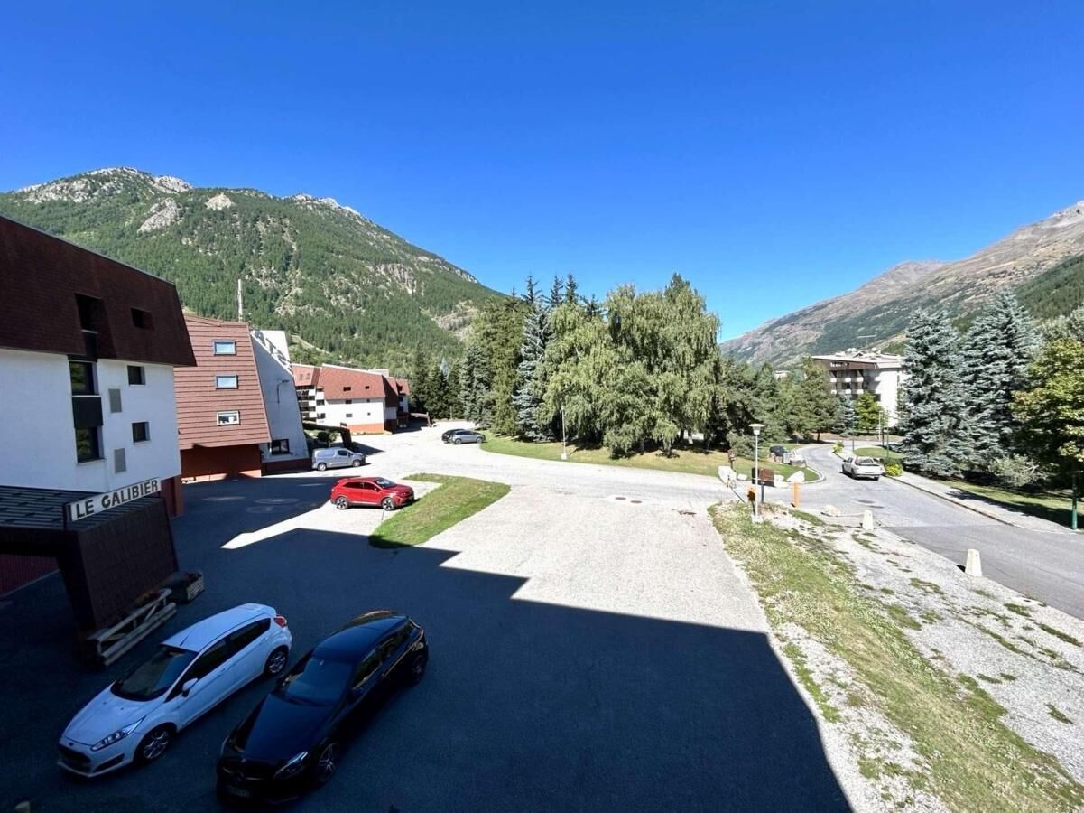 Ein Parkplatz mit mehreren Autos, ein Gebäude mit der Aufschrift 'LE GALIBIER' und einer gebirgigen Kulisse.