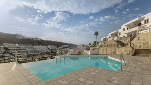 A swimming pool with a stone deck, a staircase leading to a building, and a view of a hillside with buildings. - Cumana 2 Apartment with Terrace (Puerto Rico)
