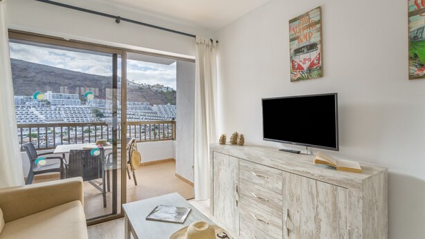 A modern living room with a television, a dining table, and a balcony with a view of buildings. - Cumana 2 Apartment with Terrace (Puerto Rico)