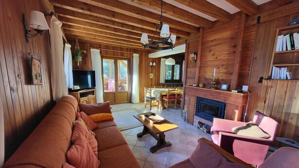 A cozy log cabin interior with a large sofa, a dining area, and a fireplace.