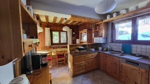A wooden cabin-style kitchen with a dining area, wooden cabinets, a tiled floor, and a window overlooking the outdoors.