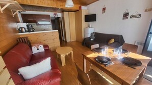 A cozy cabin-style room with a red leather sofa, a wooden dining table set for four, a small wooden stool, and a television mounted on the wall. - 300m from ski slopes, Ground floor, view parking, terrace, parking, tv, ski locker, 29m² (Montgenèvre)