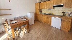 A compact kitchen with wooden cabinets, a white refrigerator, a dishwasher, and a dining table with chairs. - 300m from ski slopes, Ground floor, view parking, terrace, parking, tv, ski locker, 29m² (Montgenèvre)