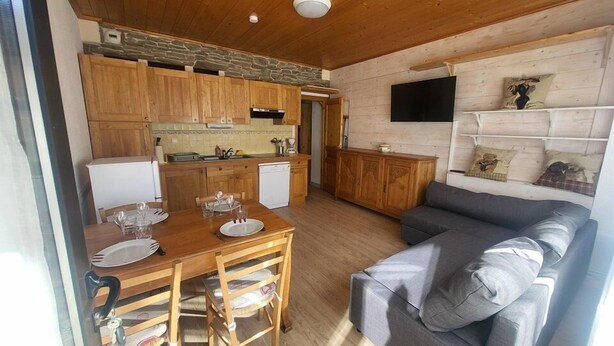 A cozy living area with a wooden dining table set for four, a grey sofa, and a kitchen with wooden cabinets and a stone accent wall. - 300m from ski slopes, Ground floor, view parking, terrace, parking, tv, ski locker, 29m² (Montgenèvre)