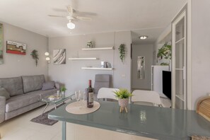 Una sala de estar moderna con un sofá, una mesa de centro y sillas, una mesa de comedor con una planta y un ventilador de techo.