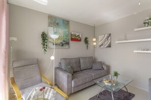Een moderne woonkamer met een grijze bank, een gele fauteuil, een glazen salontafel en een schilderij aan de muur.