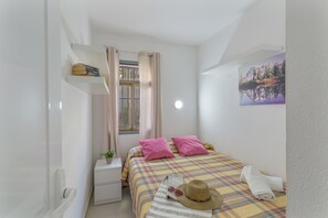Een slaapkamer met een bed, een nachtkastje, een raam met gordijnen, een wandplank en een schilderij.