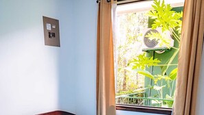 Una cama individual con colchón y almohadas azules, cabecera de madera, ventana con cortinas y un equipo de aire acondicionado instalado en la pared.