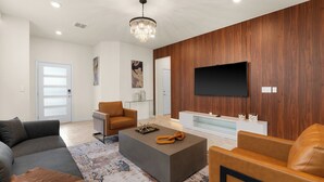 Una sala moderna con un televisor de pantalla plana grande montado en una pared de madera, un sofá gris, un sillón de cuero marrón y una mesa de centro con objetos decorativos.