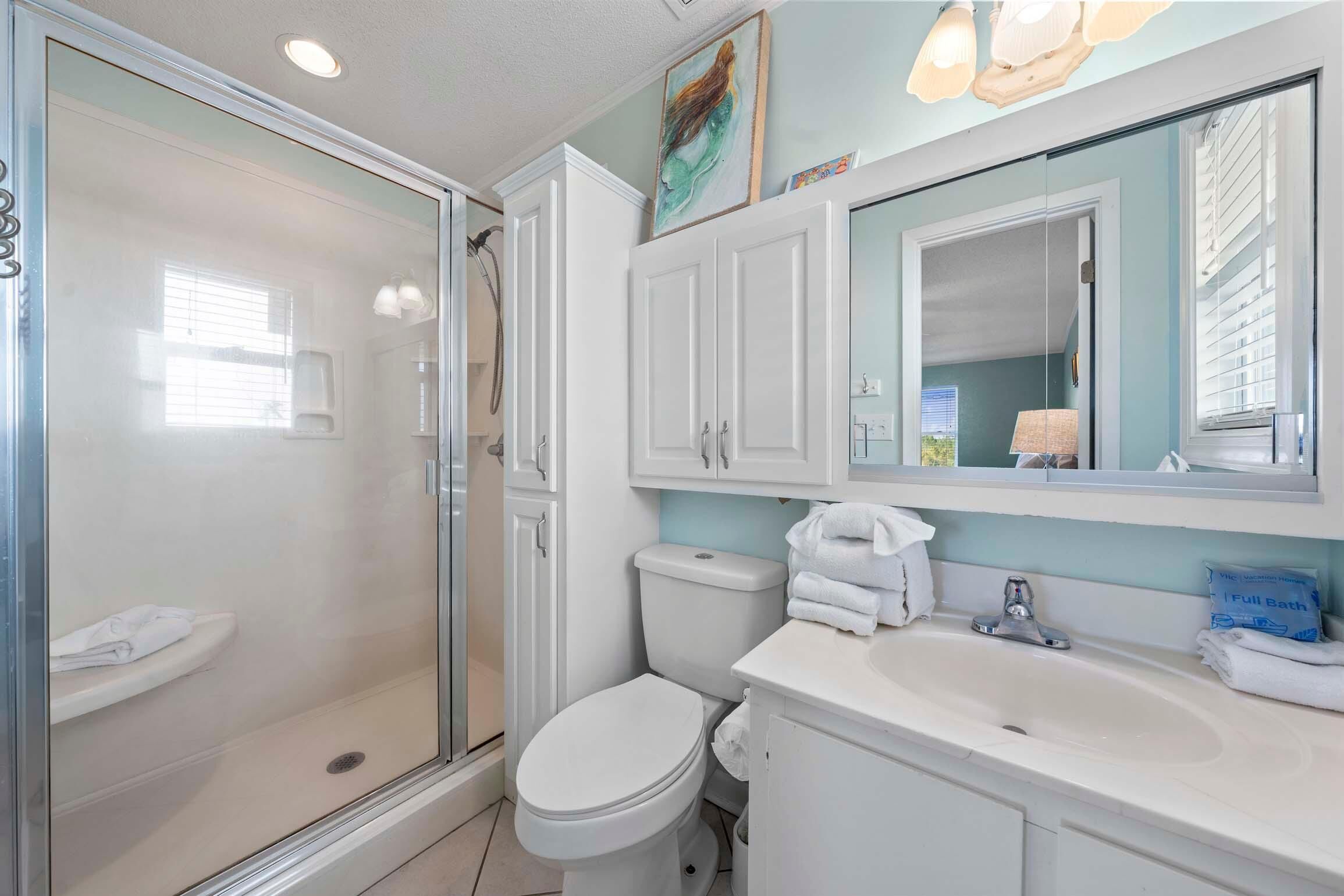 A modern bathroom with a glass shower enclosure, a white toilet, and a sink with a mirror above.