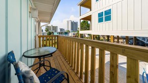 A balcony with a wooden deck, a glass table, and a blue chair. - Sands of Time (Gulf Shores)