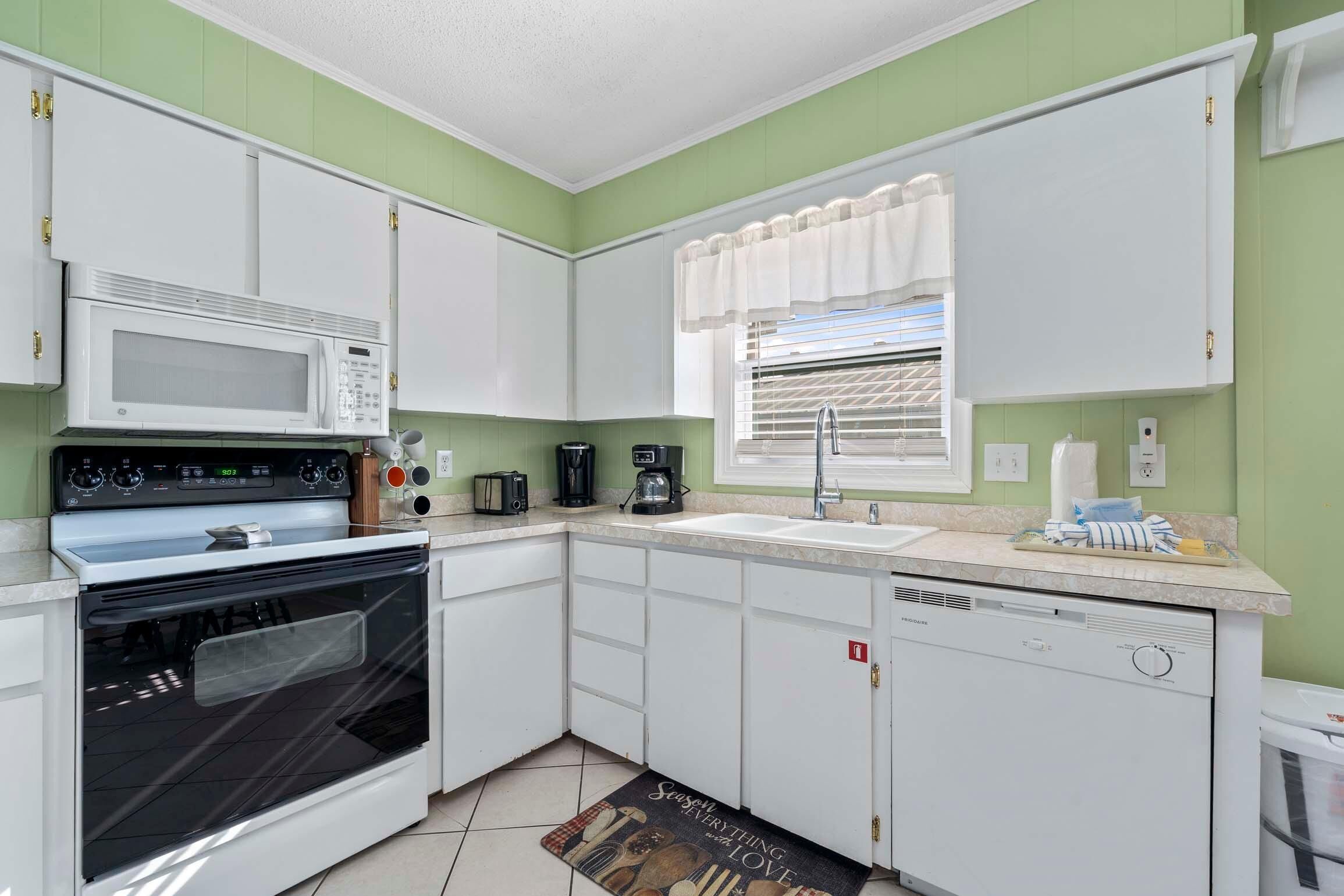 A compact kitchen with white cabinets, a microwave, a stove, a coffee maker, and a sink.