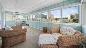 A sunroom with wicker furniture, large windows, and a view of buildings. - Sands of Time (Gulf Shores)