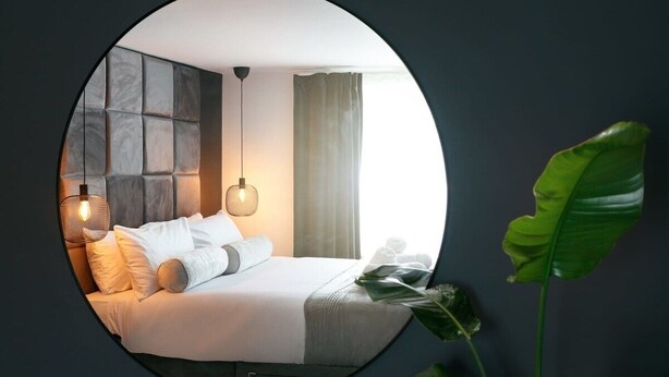 A circular mirror reflecting a modern bedroom with a bed, pillows, and a hanging light fixture. - The Luxe Experience House | Central Plymouth | Sleeps 9 (Plymouth)