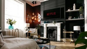 A modern living room with a fireplace, a television displaying 'NETFLIX', and a cozy seating area. - The Luxe Experience House | Central Plymouth | Sleeps 9 (Plymouth)
