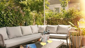 A modern outdoor seating area with a grey sofa and a table, a drink in a glass, and a bottle of champagne. - The Luxe Experience House | Central Plymouth | Sleeps 9 (Plymouth)