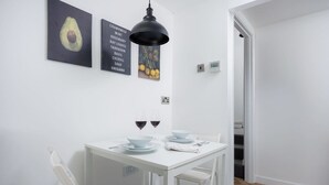 Un comedor blanco con una mesa preparada para dos, dos copas de vino tinto y una lámpara colgante negra.