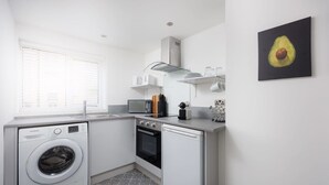 Cocina compacta con lavadora, horno, microondas y una pequeña encimera con diversos utensilios de cocina.