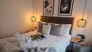 Una cama bien hecha con almohadas, una bandeja de comida y toallas. Hay una pequeña mesa con una planta y un control remoto.