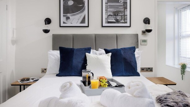 Een hotelkamer met een bed, een dienblad met handdoeken, een ontbijttafel en twee ingelijste foto's aan de muur.